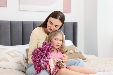 Photo of Mother and her daughter with bouquet of lilac flowers at home