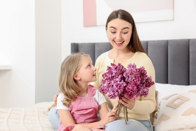 Photo of Mother and her daughter with bouquet of lilac flowers at home
