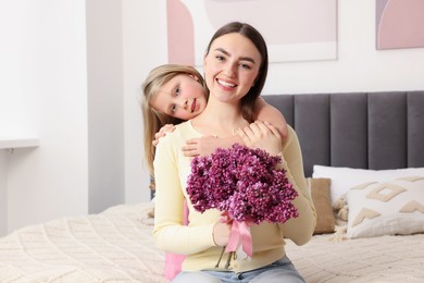 Photo of Mother and her daughter with bouquet of lilac flowers at home