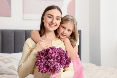 Photo of Mother and her daughter with bouquet of lilac flowers at home