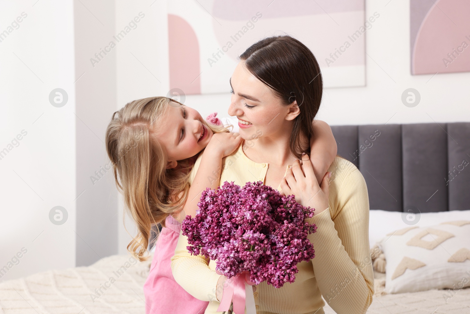Mother and her daughter with bouquet of lilac flowers at home Photo of Mother and her daughter with bouquet of lilac flowers at home