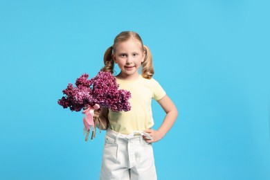 Photo of Little girl with bouquet of lilac flowers on light blue background