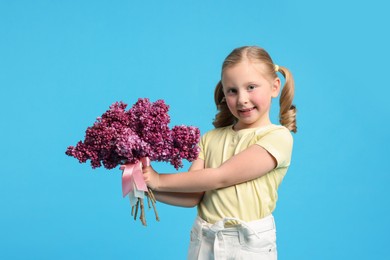 Photo of Little girl with bouquet of lilac flowers on light blue background