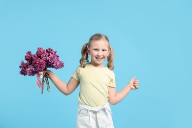 Photo of Little girl with bouquet of lilac flowers showing thumbs up on light blue background