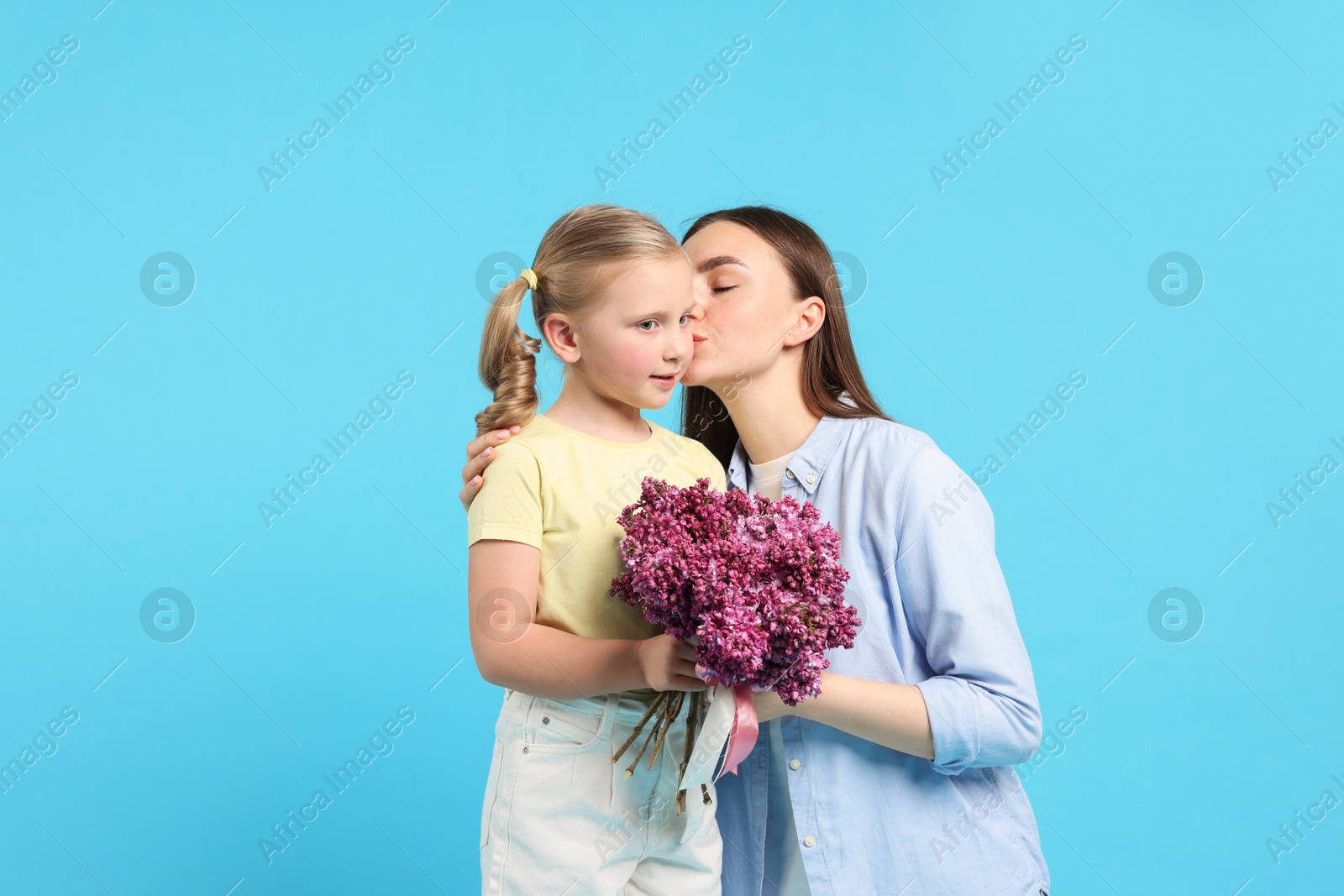 Mother and her daughter with bouquet of lilac flowers on light blue background Photo of Mother and her daughter with bouquet of lilac flowers on light blue background