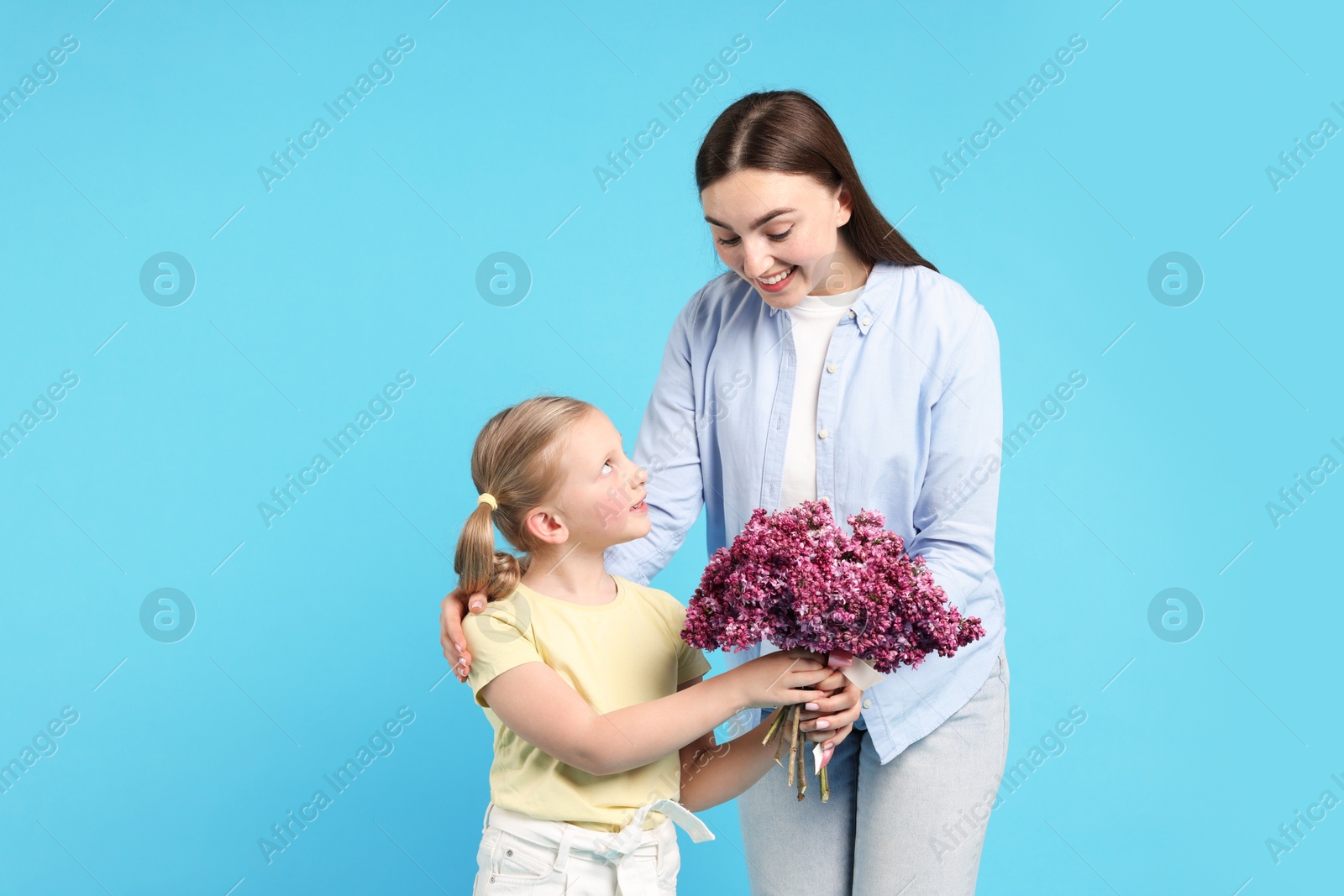 Mother and her daughter with bouquet of lilac flowers on light blue background Photo of Mother and her daughter with bouquet of lilac flowers on light blue background
