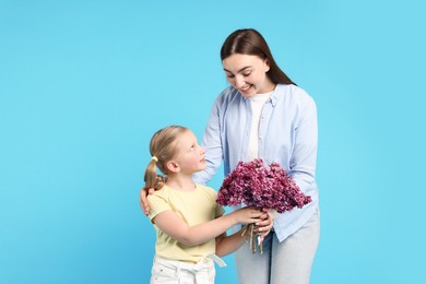Photo of Mother and her daughter with bouquet of lilac flowers on light blue background
