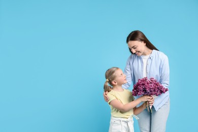 Photo of Mother and her daughter with bouquet of lilac flowers on light blue background, space for text
