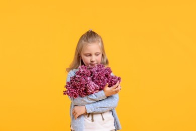 Photo of Little girl with bouquet of lilac flowers on yellow background