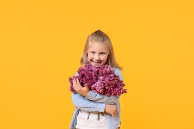 Photo of Little girl with bouquet of lilac flowers on yellow background