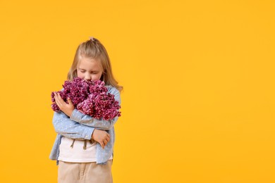 Photo of Little girl with bouquet of lilac flowers on yellow background, space for text