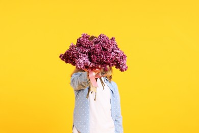 Photo of Little girl with bouquet of lilac flowers on yellow background