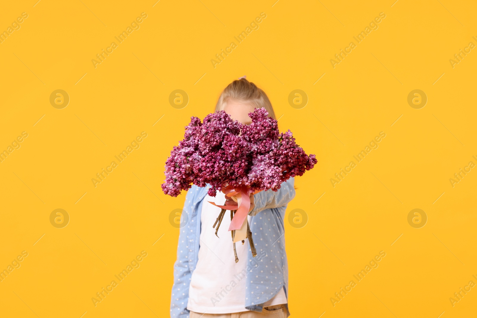 Little girl with bouquet of lilac flowers on yellow background Photo of Little girl with bouquet of lilac flowers on yellow background
