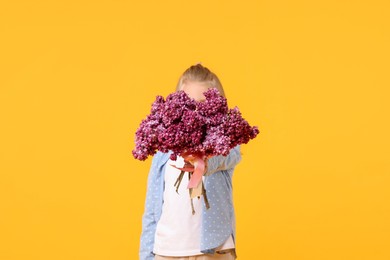 Photo of Little girl with bouquet of lilac flowers on yellow background