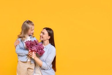 Photo of Mother and her daughter with bouquet of lilac flowers on yellow background, space for text