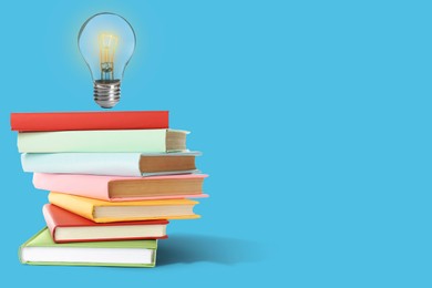Image of Idea and knowledge. Light bulb in air over stack of books on light blue background, space for text