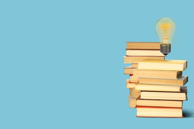 Image of Idea and knowledge. Light bulb in air over stack of books on light blue background, space for text