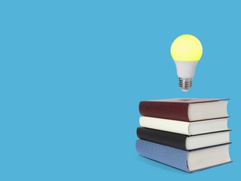 Image of Light bulb in air over stack of books on light blue background, space for text. Idea and knowledge