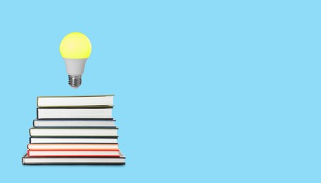 Image of Idea and knowledge. Light bulb in air over stack of books against light blue background, space for text. Banner design