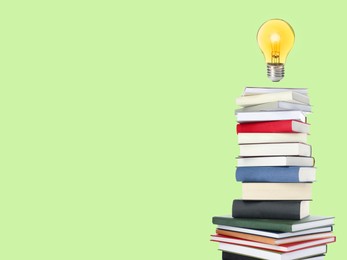 Image of Light bulb in air over stack of books on light green background, space for text. Idea and knowledge