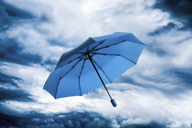 Image of Blue umbrella flying in cloudy sky. Stormy weather
