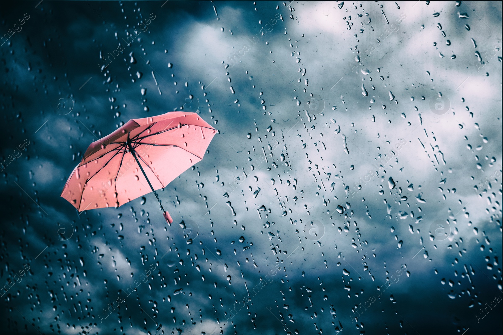 Pink umbrella flying in dark cloudy sky, view through wet window. Stormy weather Image of Pink umbrella flying in dark cloudy sky, view through wet window. Stormy weather