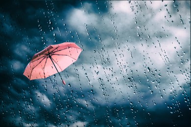 Image of Pink umbrella flying in dark cloudy sky, view through wet window. Stormy weather