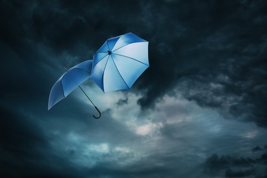 Image of Blue umbrellas flying in dark cloudy sky. Stormy weather