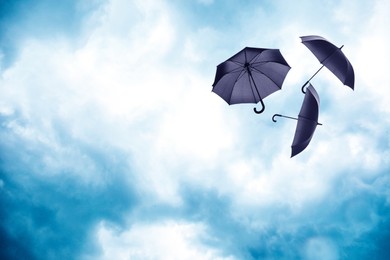 Image of Black umbrellas flying in cloudy sky. Stormy weather