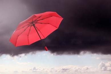 Image of Red umbrella flying in cloudy sky. Stormy weather