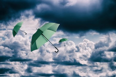 Image of Green umbrellas flying in cloudy sky. Stormy weather