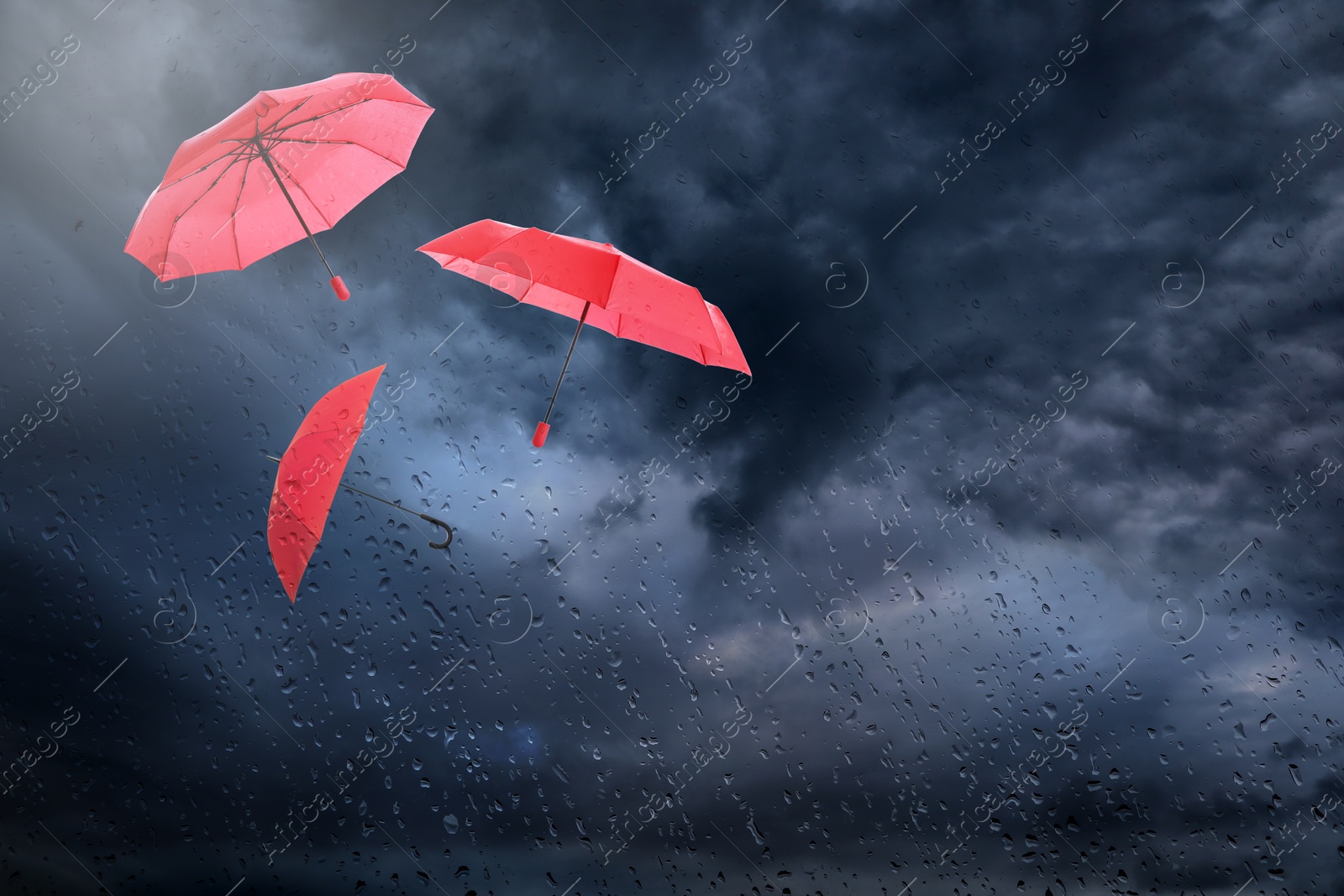 Red umbrellas flying in dark cloudy sky, view through wet window. Stormy weather Image of Red umbrellas flying in dark cloudy sky, view through wet window. Stormy weather