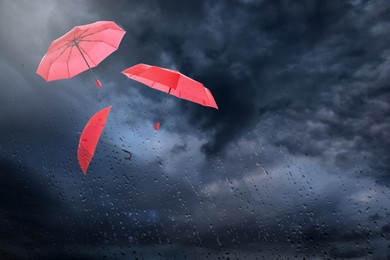 Image of Red umbrellas flying in dark cloudy sky, view through wet window. Stormy weather