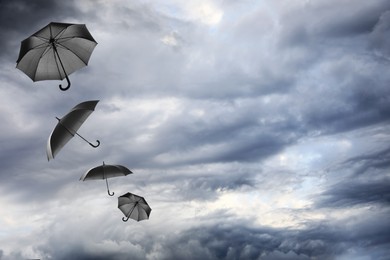 Image of Black umbrellas flying in cloudy sky. Stormy weather