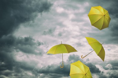Image of Yellow umbrellas flying in cloudy sky. Stormy weather