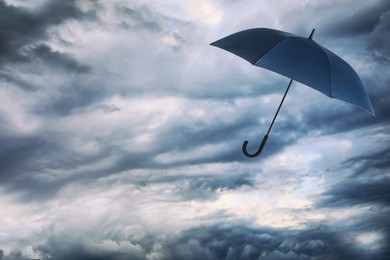 Image of Dark blue umbrella flying in cloudy sky. Stormy weather