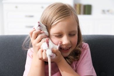 Photo of Little girl with cute white rat on sofa at home