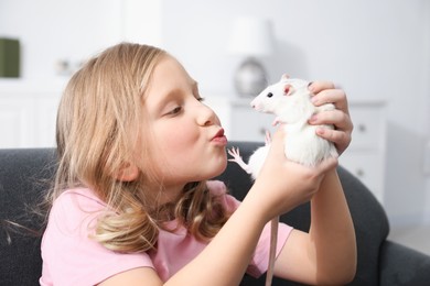 Photo of Little girl with cute white rat on sofa at home