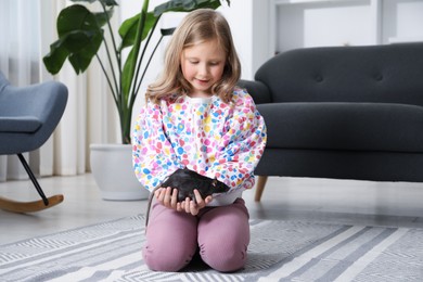 Photo of Little girl with cute black rat on floor at home