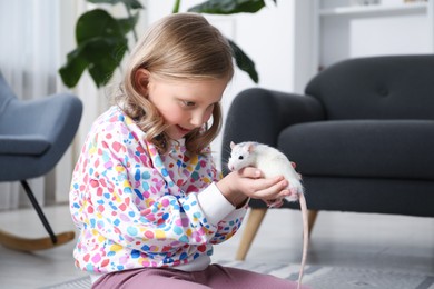 Photo of Little girl with cute white rat on floor at home
