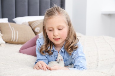 Photo of Little girl with cute white rat on bed at home
