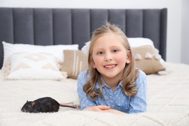 Photo of Little girl with cute black rat on bed at home