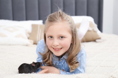 Photo of Little girl with cute black rat on bed at home