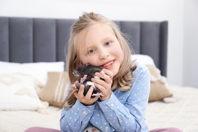 Photo of Little girl with cute black rat on bed at home