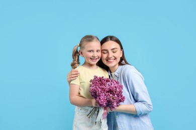 Photo of Mother and her daughter with bouquet of lilac flowers on light blue background