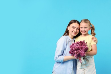 Photo of Mother and her daughter with bouquet of lilac flowers on light blue background, space for text