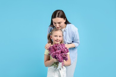 Photo of Mother and her daughter with bouquet of lilac flowers on light blue background