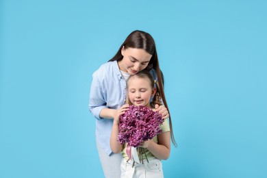 Photo of Mother and her daughter with bouquet of lilac flowers on light blue background