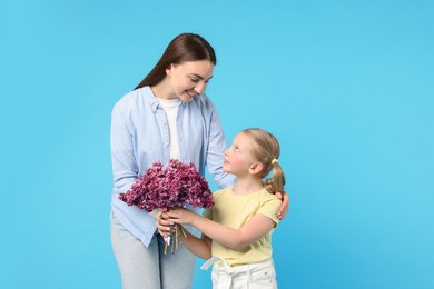 Photo of Mother and her daughter with bouquet of lilac flowers on light blue background