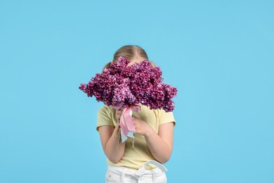 Photo of Little girl with bouquet of lilac flowers on light blue background